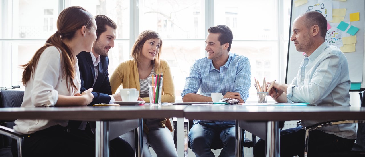 Five people are sitting around a desk in an office and talk about business.